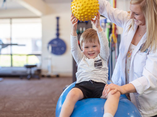 Child lifting a ball as a part of physical therapy with a physicial therapist